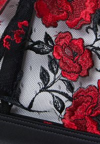 Black mesh fabric featuring red embroidered roses with black leaves. The design includes intricate detailing and a smooth black trim.