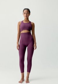 Atletisk set i djup lila, bestående av en kort sportbh och högmidjade leggings med strukturerade mönster och sömlös design.