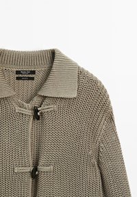 Cardigan en coton beige tricoté avec un col à revers, présentant un tissage texturé, une fermeture à bascule à l'avant et deux boutons foncés.