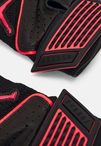 Sorte træningshandsker med struktureret sort stof, røde accenter og perforerede detaljer. Har gummieret rustning og præget branding.