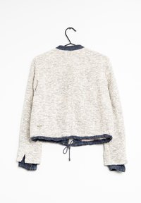 Kremowa kurtka o strukturze z kołnierzem dżinsowym, krótki fason i ściągacz u dołu. Posiada rękawy raglanowe i prosty, casualowy styl.