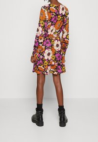 Blumenkleid mit langen Ärmeln, das orangefarbene, rosa und weiße Blumen auf schwarzem Hintergrund zeigt. Abgerundet mit einem Rüschen-Saum und einem elastischen Taillenbund.