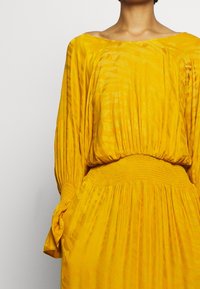 Yellow dress with a relaxed neckline, gathered waist, and textured fabric. Features long, billowy sleeves and subtle pattern detailing.