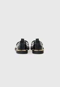 Zwarte gepatineerde leren sandalen met uitsnijdingen, goudaccenten op de hak en trekbandjes. Gladde textuur met minimalistische stijl.