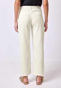 Bílé široké džíny s vysokým pasem a uvolněným střihem, se zadními kapsami. Materiál vypadá měkký a má hladkou strukturu.