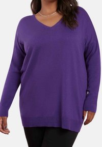 Lila långärmad V-ringad tröja med avslappnad passform, ribbade manschetter och en mjuk textur, i kombination med svarta byxor.