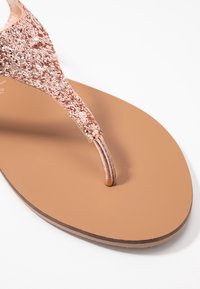 Roze gouden glitter flip-flops met een dunne band, een ronde neus en een gladde bruine zool. Heeft een plat ontwerp dat geschikt is voor casual gebruik.