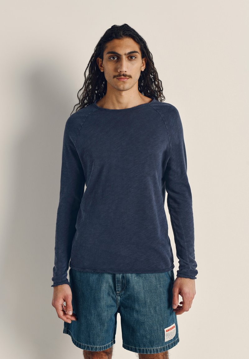 Tamsiai mėlyna ilgomis rankovėmis marškiniai su apvalia iškirpte ir raglan rankovėmis, pagaminti iš minkštos medžiagos. Suderinti su džinsiniais šortais su logotipo užsegimu.