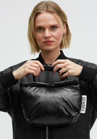 Schwarze gesteppte Schultertasche mit glatter Textur und gerafftem oberen Teil. Verfügt über ein Etikett an der Seite mit der Aufschrift "SENSES" und ein kompaktes Design.