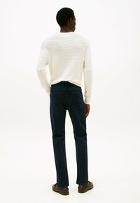 Jeans de color azul oscuro con corte recto, combinados con un suéter blanco a rayas, vistos desde la parte de atrás. Tejido suave, con detalles mínimos.