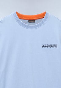 Light blue t-shirt with an orange ribbed neckline and black graphic text "NAPAPIJRI geographic" on the chest. Soft cotton material.