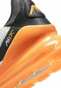 Černobílé tenisky s oranžovou podrážkou. Obsahují texturovanou tkaninu a tvarovanou patu. Branding "Air" v bílé a oranžové barvě.