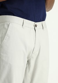 Pantalones de algodón beige con corte ajustado, cierre de cremallera y botón. Con bolsillos laterales y una textura suave.