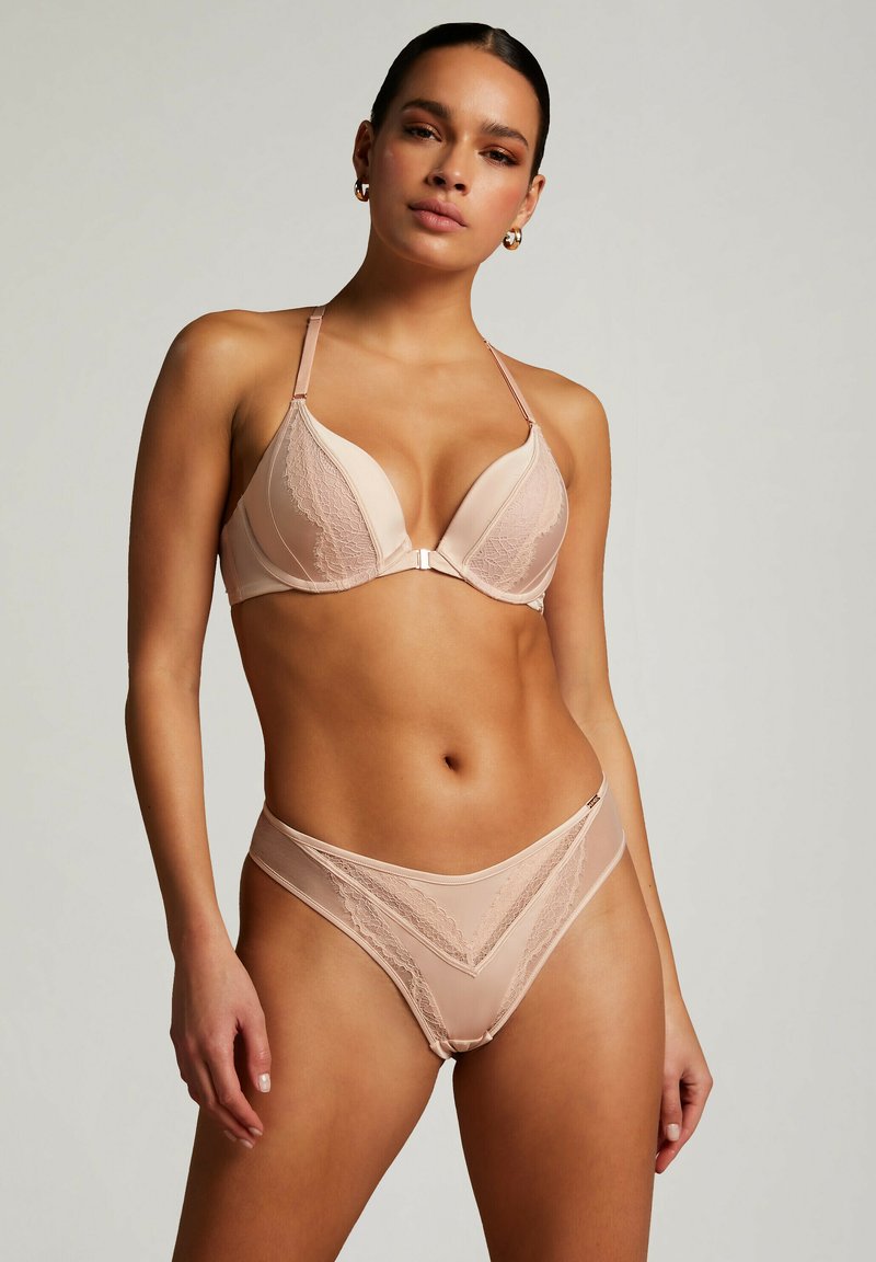Bh og bikini sæt i nude. Bh'en har polstrede skåle, blonde detaljer og justerbare stropper. Bikini har en v-formet udskæring med blonde accenter.