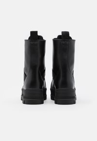 Bottes basses en cuir noir avec une finition lisse, panneaux latéraux élastiques et semelles en caoutchouc épaisses. Boucles pour un enfilage facile.