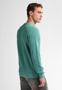 Turquoise gebreid shirt met lange mouwen en een ronde hals, met een gestructureerd patroon en aansluitende mouwen, gecombineerd met grijze denim jeans.