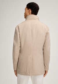 Beige wollen jas met een hoge kraag, rechte snit en zichtbare naden. Beschikt over een achterste split en zijzakken. Gelaagd materiaal.