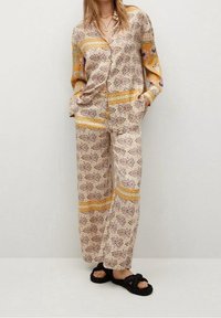 Ensemble pyjama deux pièces en tissu crème clair présentant des motifs floraux et géométriques, des rayures jaunes, des manches longues et un pantalon ample.