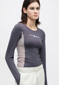 Αθλητική μπλούζα μακρυμάνικη σε γκρι-μωβ χρώμα με πιο ανοιχτές πλευρικές ταινίες, λεία υφή και λογότυπο Nike στο στήθος.