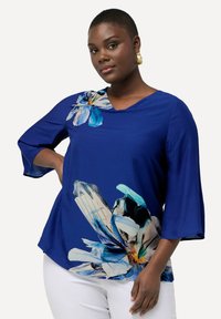 Blusa blu con design floreale dai colori vivaci. Scollo a V, maniche a tre quarti, vestibilità leggermente ampia, realizzata in tessuto leggero.