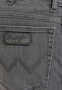 Grå denimtyg har en Wrangler-läderetikett på bakfickan, med ett zigzag-sticks mönster ovanför fickan.