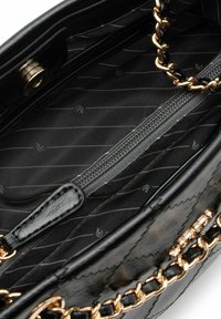 Schwarzes Handtaschen-Innenleben mit gesteppter Textur, goldfarbenen Metallakzenten und einer Reißverschlusstasche vor einem gestreiften Stofffutter.