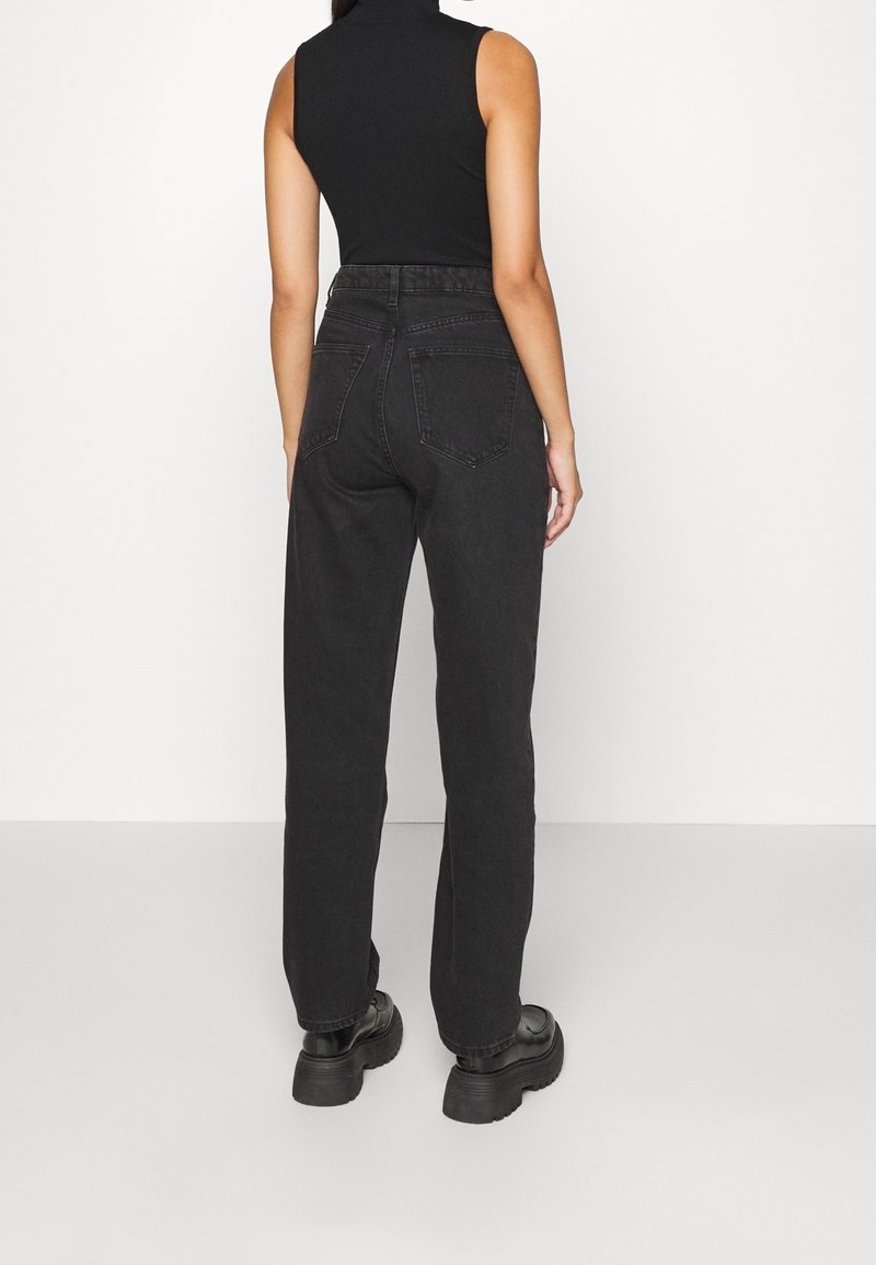 Black high-waisted jeans with a straight-leg design, made of denim, featuring two back pockets. Worn with chunky black platform boots.