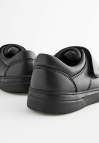 Black leather shoes with thick soles and Velcro straps, shown from a low rear angle on a white background.