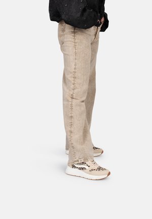 Beige denim jeans met rechte pijpen, gecombineerd met beige en dierenprint sneakers die een textuurmateriaal en een contrasterende zool hebben.