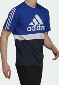 Camiseta azul y marino de Adidas con una franja horizontal blanca y logo. Presenta tres franjas blancas en los hombros. Mezcla de algodón, cuello redondo.