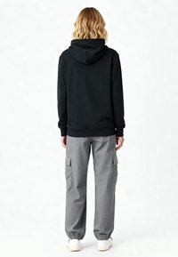 Sweatshirt noir à capuche avec des poignets côtelés, associé à un pantalon cargo gris ample comportant des poches latérales et des poignets de cheville élastiqués. Baskets blanches.