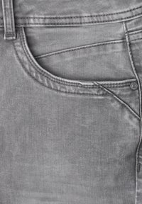 Gros plan d’un jean en denim gris montrant la poche avant, les coutures, la ceinture avec passants et un détail de rivet en métal.