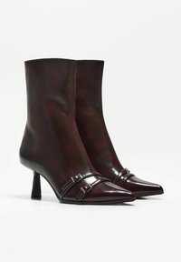 Bordowe skórzane botki za kostkę z cienkim noskiem, ozdobione błyszczącymi paskami i klamrami, z umiarkowanym obcasem typu stiletto.