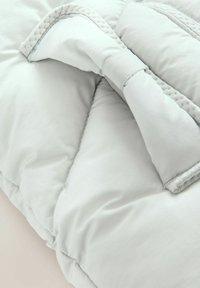 Gaiši pelēks quiltēts gultas pārklājs ar gludu tekstūru, ar šūtu maliņu un salocītu stūri, kas atklāj mīksto pildījumu.