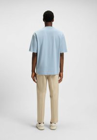 Light blue cotton T-shirt with short sleeves, round neckline, and relaxed fit. Paired with beige trousers and white sneakers.