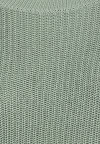 Hellgrüner, gestrickter Stoff mit einer strukturierten, gerippten Oberflächenstruktur, die diagonale Linien und ein weiches, elastisches Aussehen aufweist. Geeignet für verschiedene Anwendungen.
