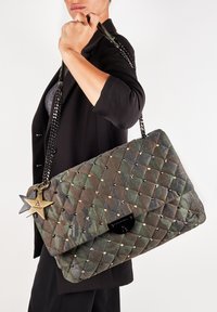 Bolso de mano acolchado en camuflaje verde con tachuelas doradas, correa de cadena negra y charms en forma de estrella. Cuenta con un cierre de solapa y una tela texturizada.