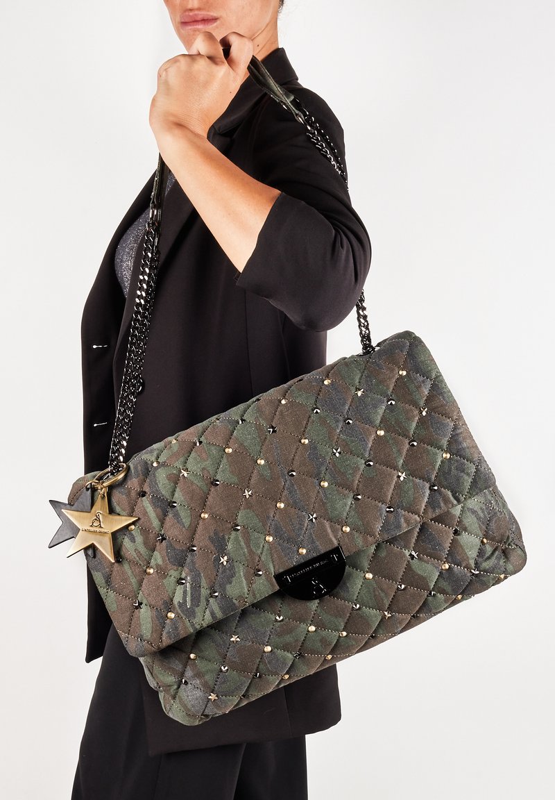 Bolso de mano acolchado en camuflaje verde con tachuelas doradas, correa de cadena negra y charms en forma de estrella. Cuenta con un cierre de solapa y una tela texturizada.