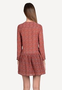 Långärmad klänning i en texturerad rödaktig tyg, med en utsvängd kjol och subtilt mönster. Stängd rygg med rund halsringning.