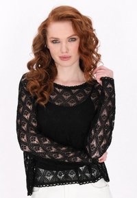 Černý krajkový top s dlouhými průhledn�ými rukávy, kulatým výstřihem a složitými diamantovými vzory. Spodní okraj je vlnkovaný s texturovaným povrchem.