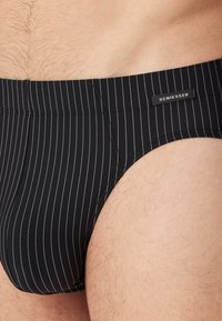Slip da bagno a strisce nere con vita piatta, caratterizzati da un'etichetta del marchio e una texture di tessuto liscia.