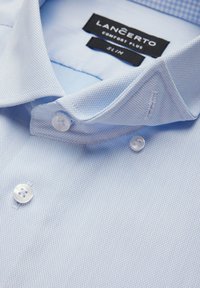 Jasnoniebieska koszula w kratę o miękkiej fakturze, z kołnierzykiem zapinanym na guziki, białymi guzikami oraz metkami pokazującymi markę i fason.