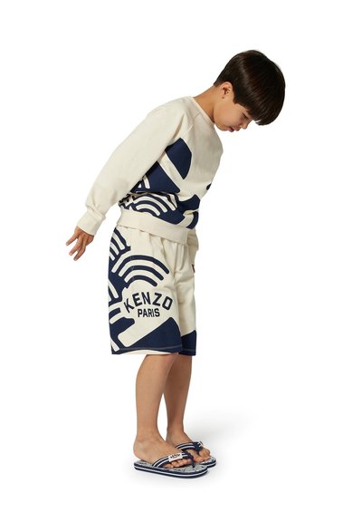 Lichtbeige sweatshirt met marineblauwe print; bijpassende beige shorts met de tekst "KENZO PARIS". Draag het met marineblauwe en witte slippers.