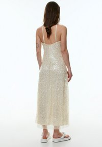 Beiges Maxikleid mit glitzernden Pailletten, dünnen Trägern und tailliertem Oberteil. Abgeschlossen mit einer fließenden, durchsichtigen Schicht am Saum.