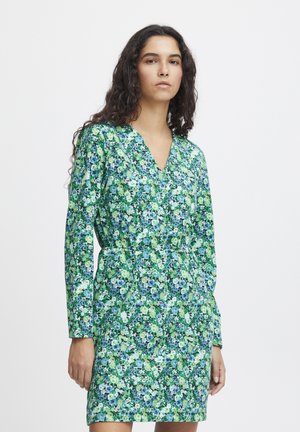Robe florale avec des motifs verts, bleus et blancs. Manches longues, décolleté en V, taille cintrée, longueur au genou, en tissu léger.