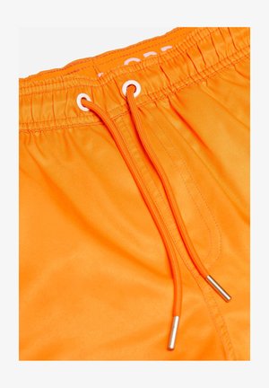 Shorts de bain orange vif avec une taille élastique, comprenant des œillets blancs et un cordon de serrage avec des embouts en métal. Tissu lisse et léger.