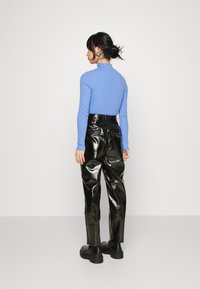 Top azul de manga longa e gola alta, combinado com calças pretas brilhantes de cintura alta e botas pretas robustas, visto de trás.