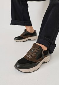 Sneaker neri, marroni e grigi che presentano una combinazione di materiali in suede e rete, con un evidente dettaglio della cerniera e una suola spessa.