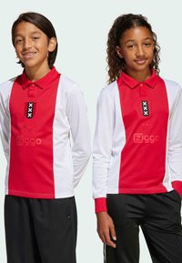 Červené a biele dlhé rukávy polo tričká s golierom, s čiernym emblémom s bielymi akcentmi a čierne športové nohavice.