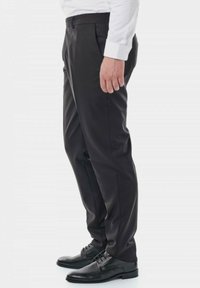 Pantalons habillés noirs avec une texture lisse, coupe slimming et taille standard, associés à des chaussures noires à lacets. Vue de profil.